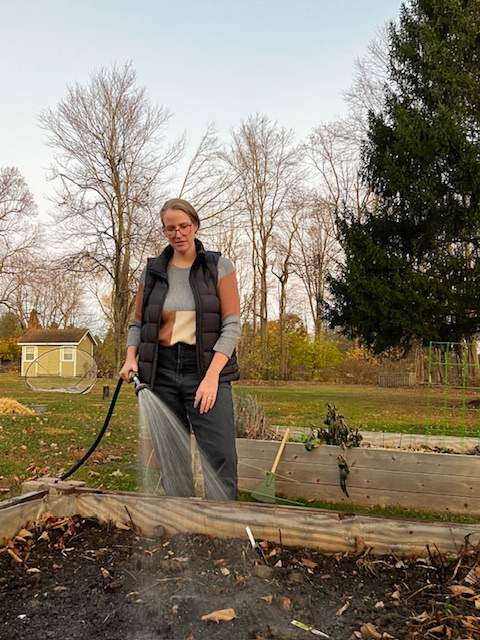 woman holding hose watering plants in raised garden bed